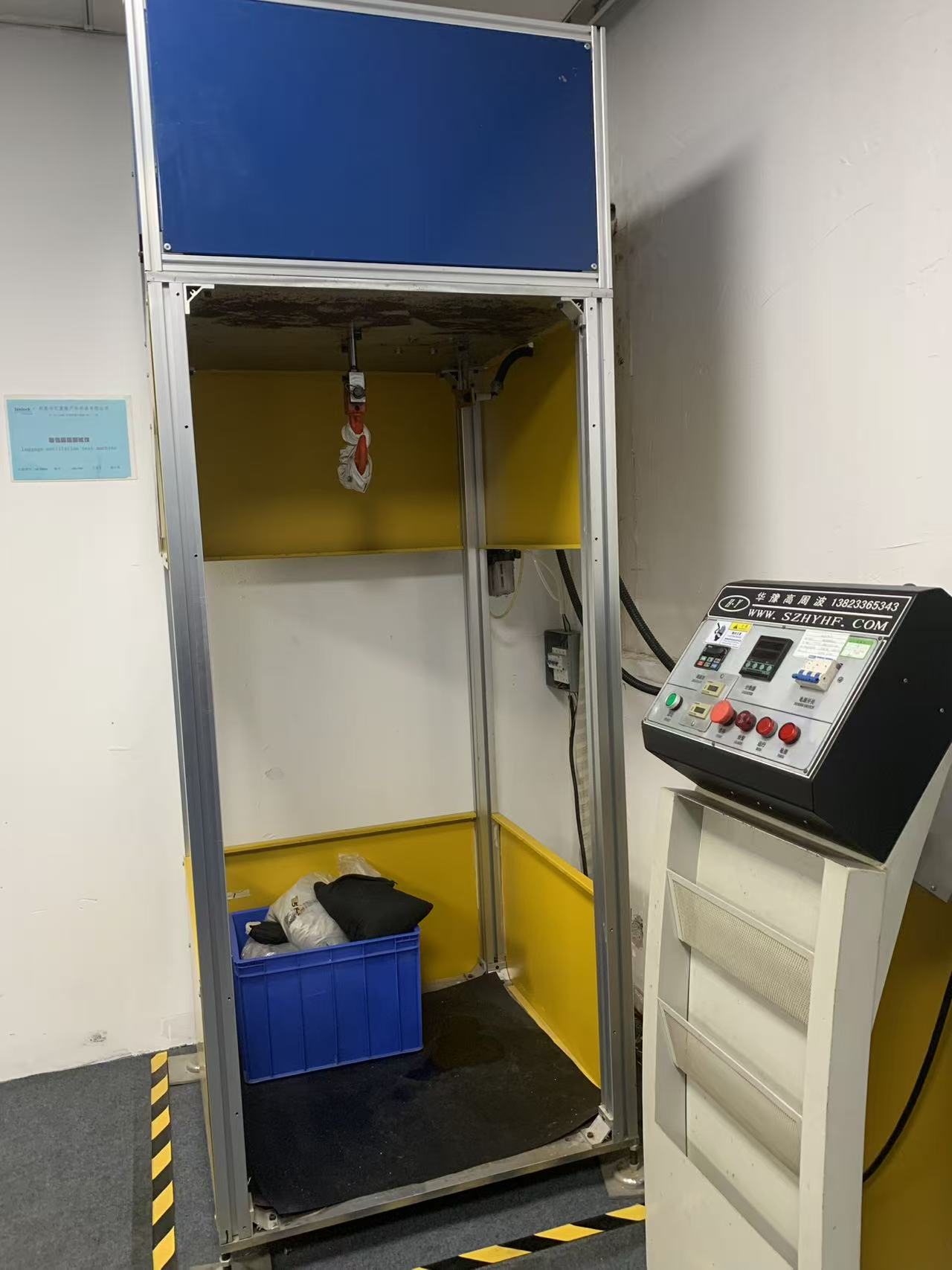 Interior of the oscillation test chamber showing the overhead impact head with fixture and the weight crate below
