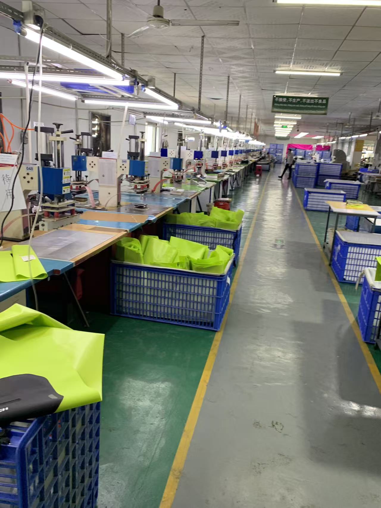 High-frequency welding line at the Sealock factory with rows of welding machines and crates of fluorescent yellow waterproof fabric